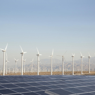 Many wind turbines and a large solar panel array in a desert valley, mountains in the distance and blue sky above. Palm Springs, California, USA
